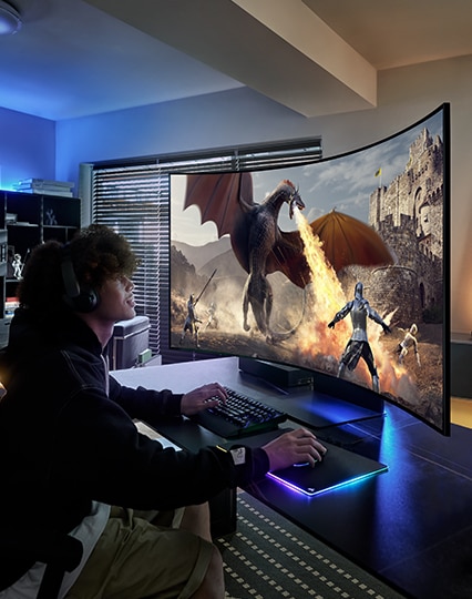 A man is playing a game with a monitor. There're a dragon and some people in the game scene.