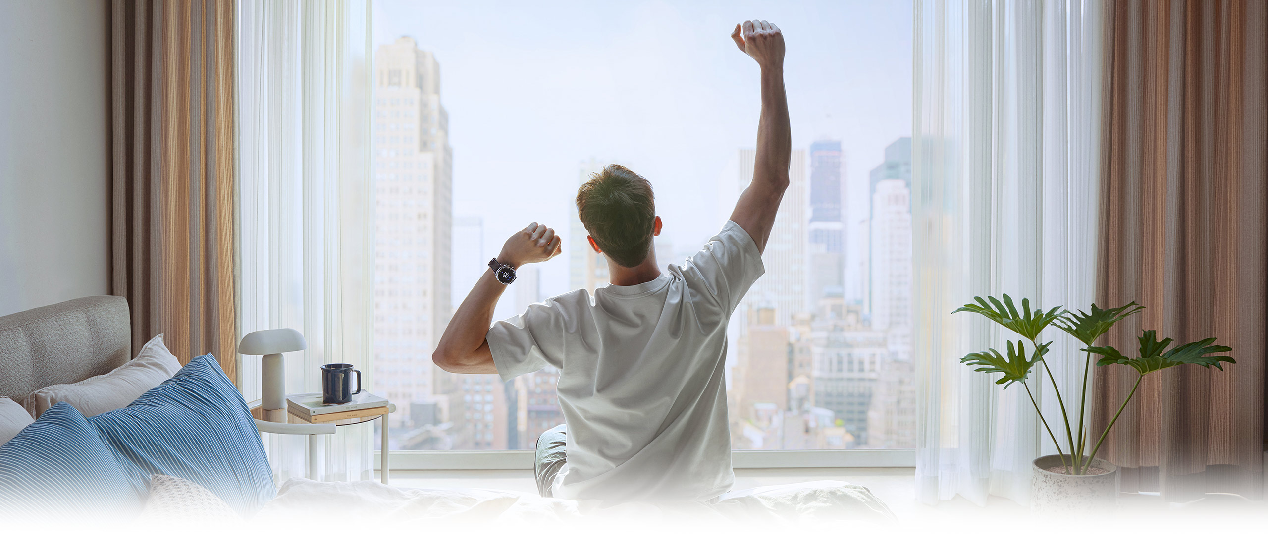 清晨，一位人士面朝窗户，正在伸展手臂。一只手腕上佩戴着Galaxy Watch8 Classic。
