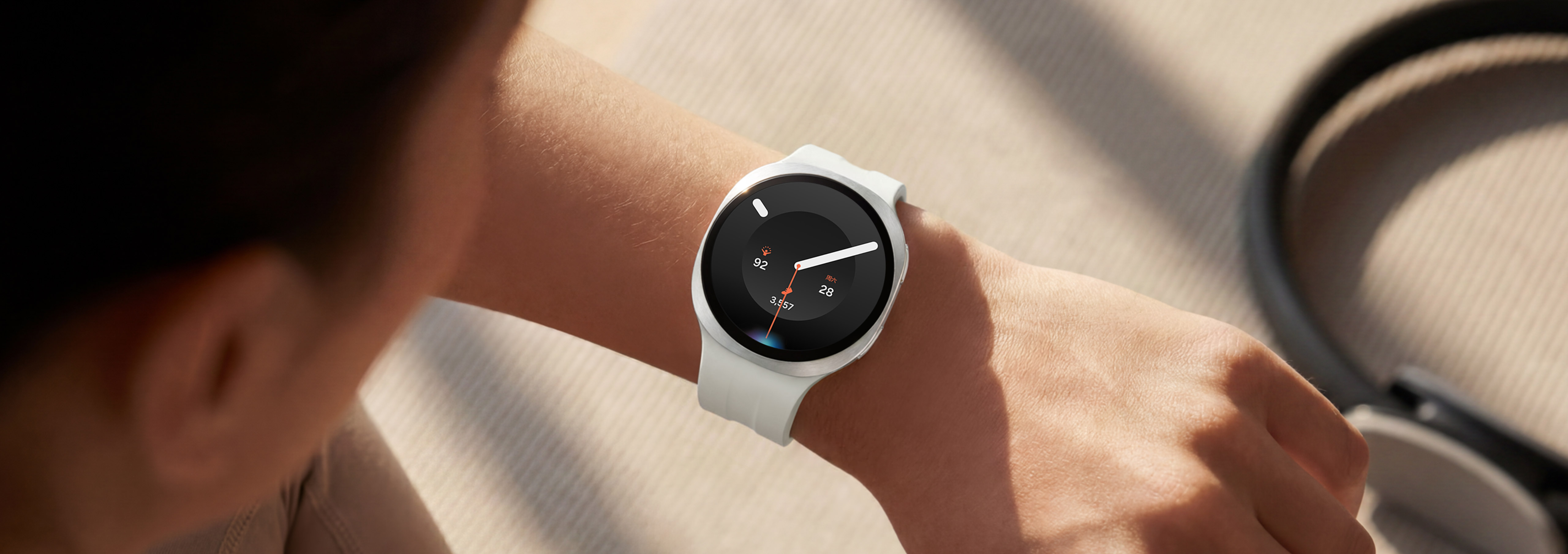 画面中的骑行人物佩戴一块Galaxy Watch9，这款手表搭配白色运动表带。用户抬起手腕，通过Bixby向手表下达语音命令。