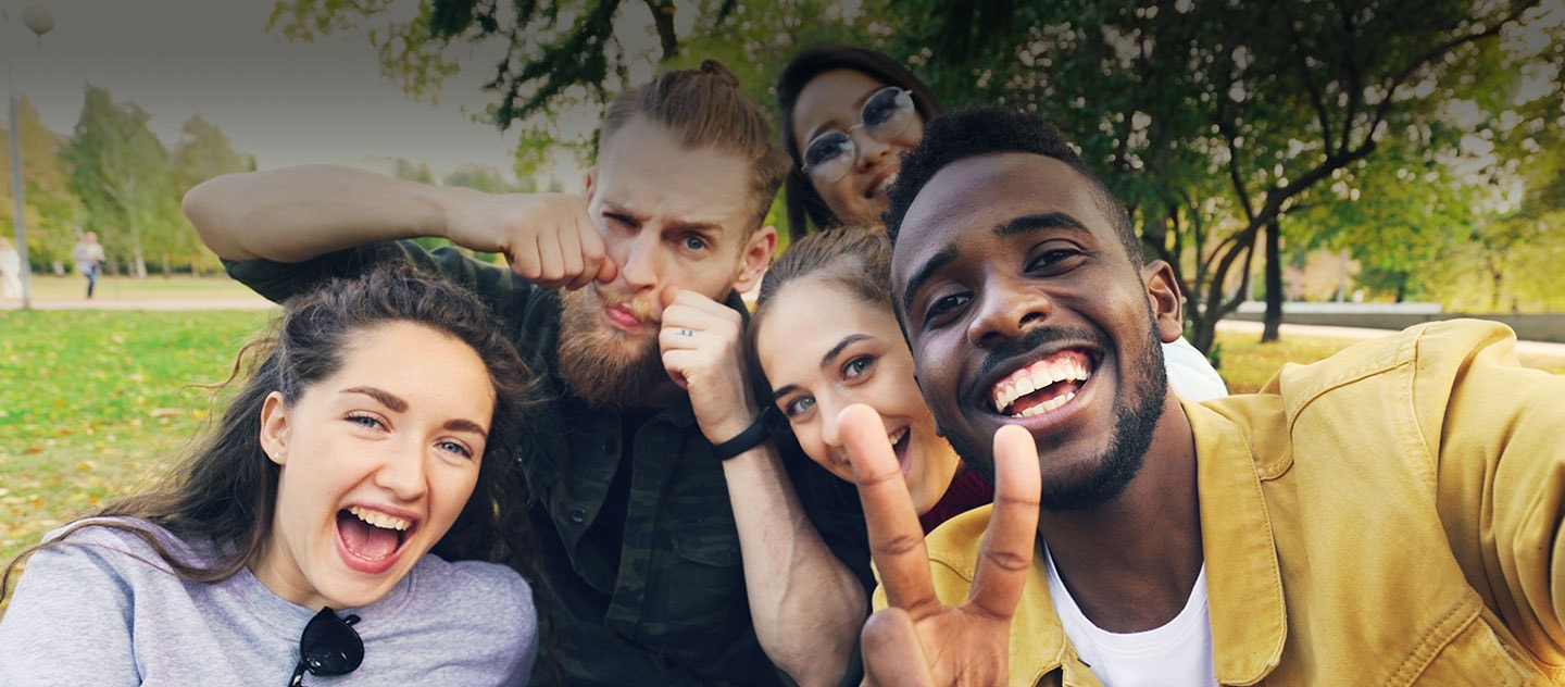 Five people smiling and taking a selfie together in a park.